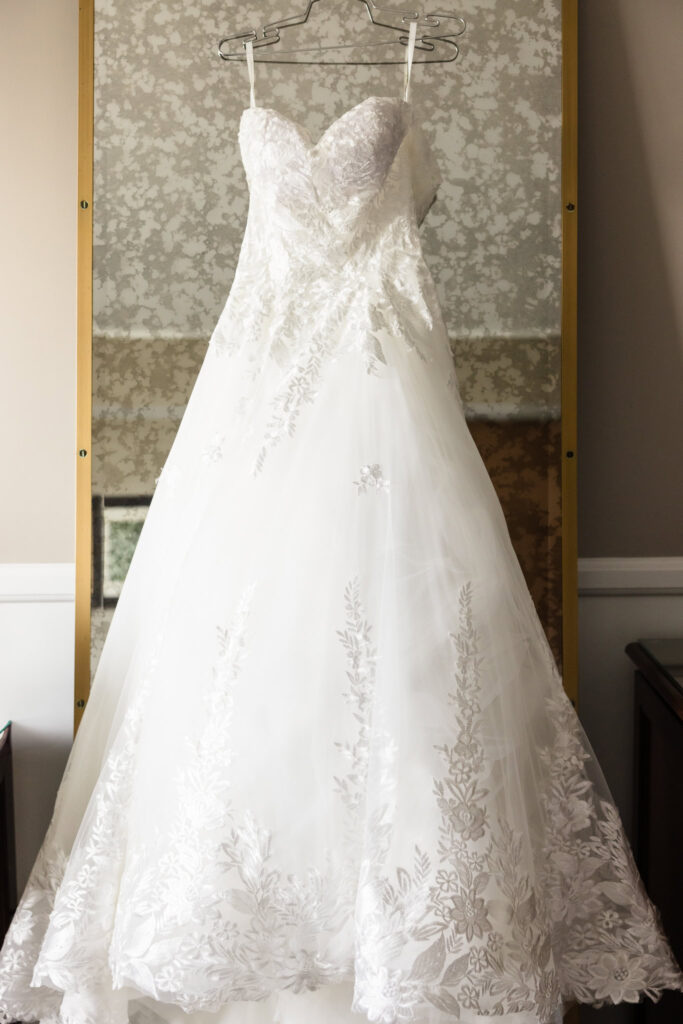 Full length image of bride's wedding dress hanging on mirror at Garden City Hotel.