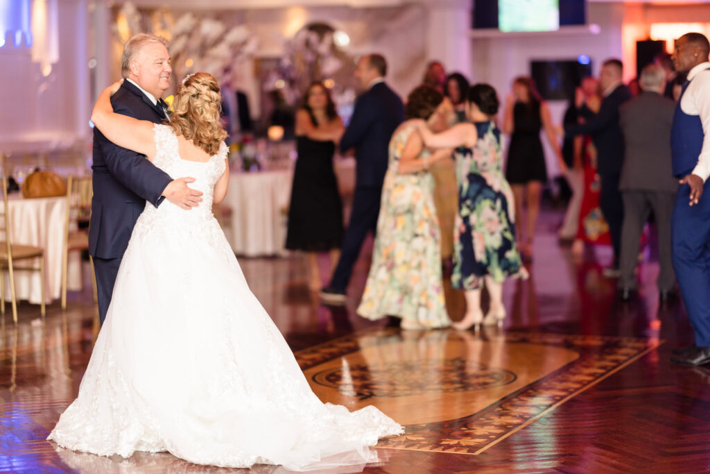 Bride and groom dancing alone at Sand castle while other guests are in the back.