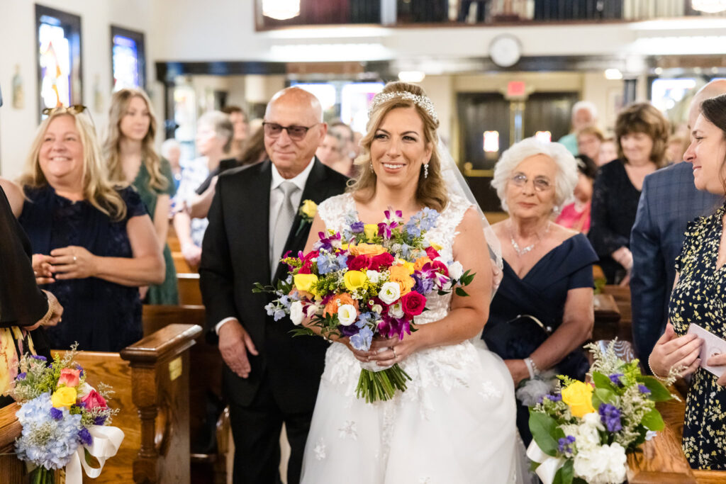 Bride walking down the aisle with colorful bouquet.