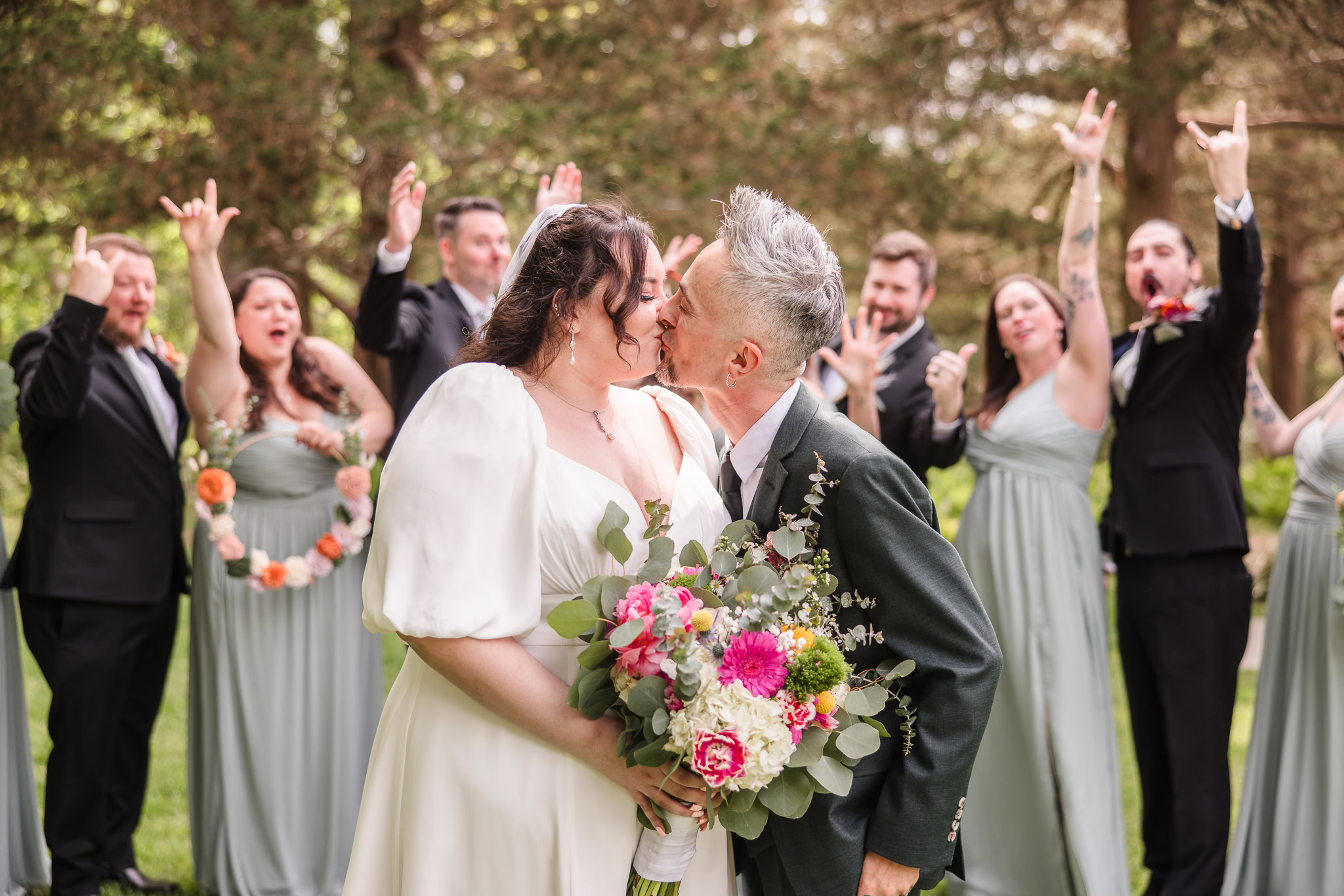 Bride and groom kissing in front of bridal party cheering at Bates House.