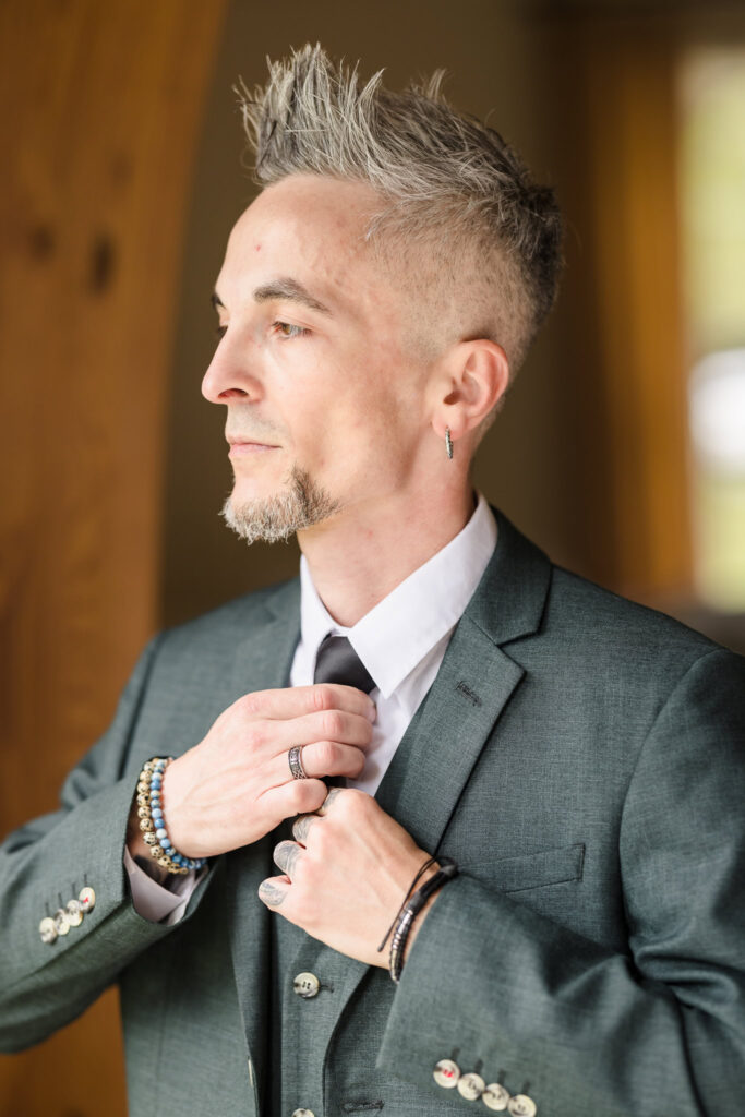 Groom in green suite adjusting his tie at Bates House in Frank Melville Park.