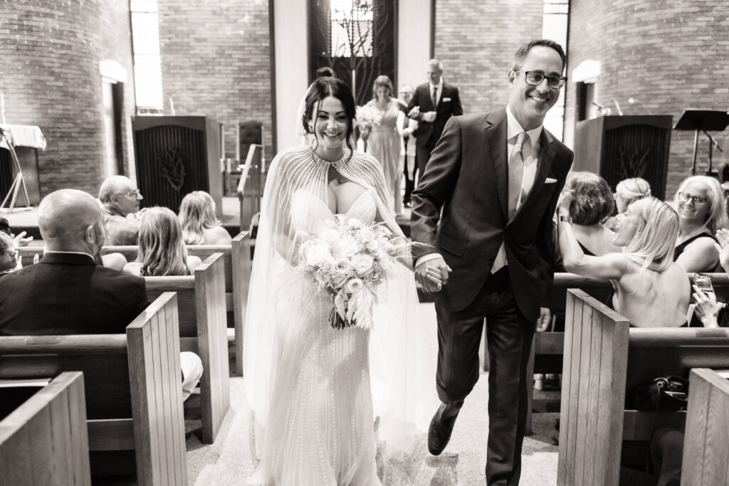 Bride and groom walking down the aisle after their wedding ceremony while smiling.