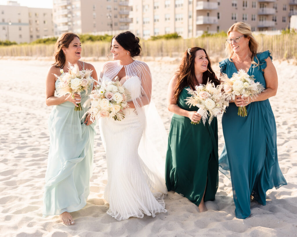 Bride and Bridesmaids walking on the sand at Long Beach while laughing and smiling. 