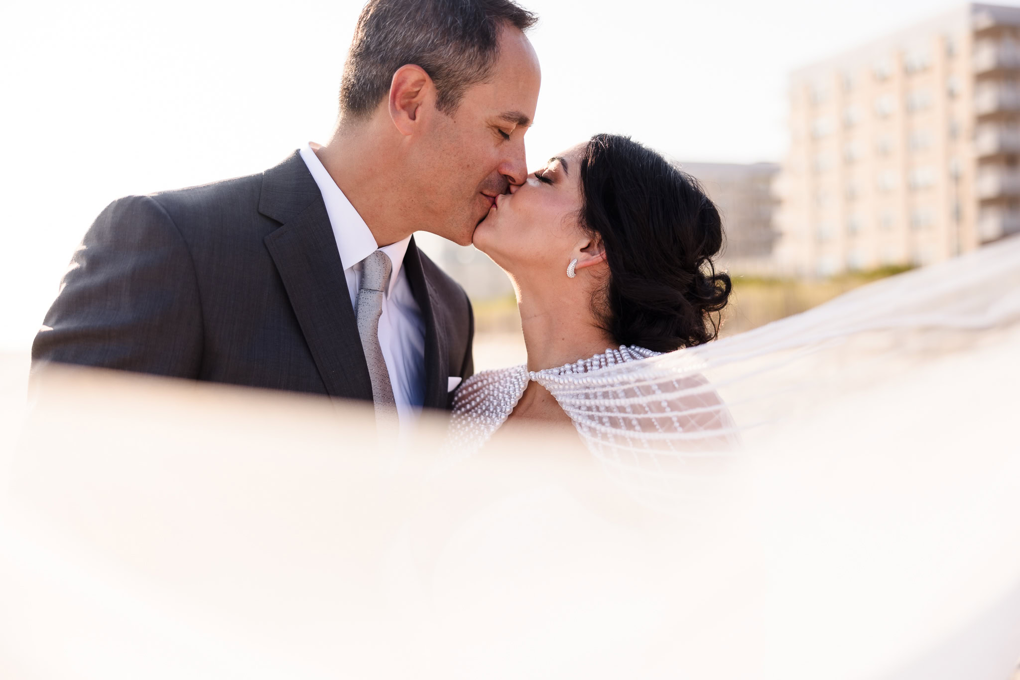 Couple kissing on Long Beach with veil coming toward the camera.