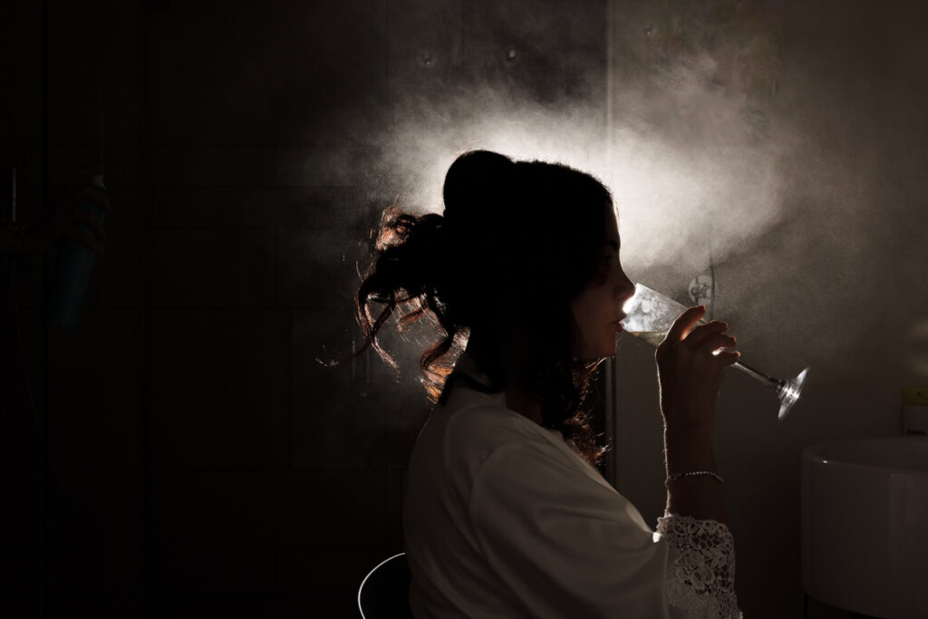 Silhouette of a bride drinking wine in a cloud of hairspray.