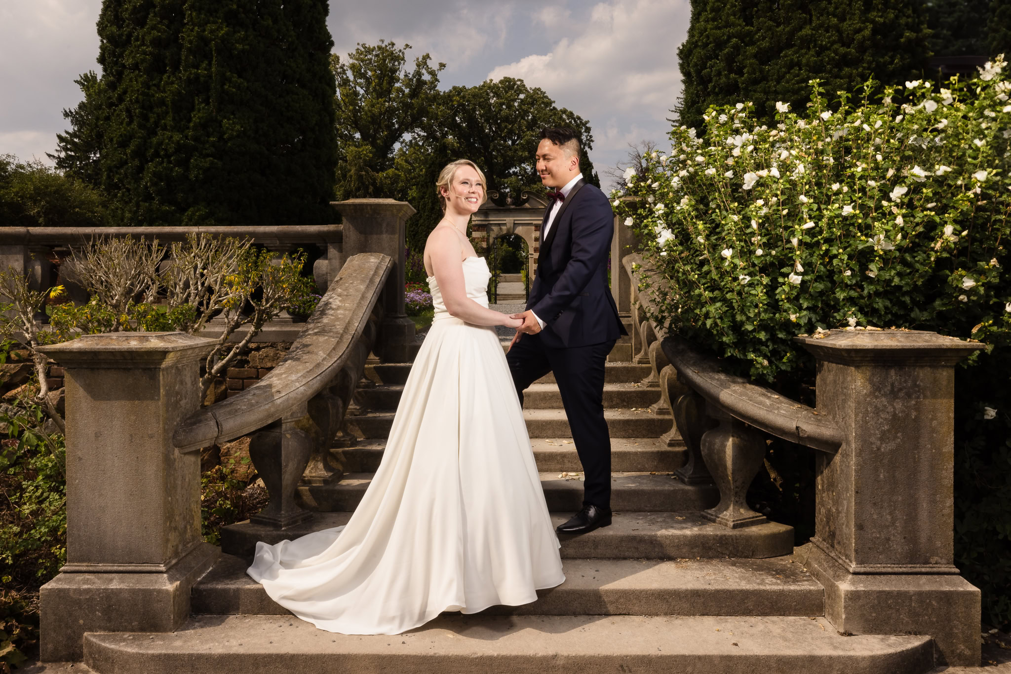 Bride and groom on staircase to Old Westbury Gardens. Groom is looking at the bride, and bride is looking off into the distance.