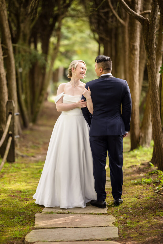 Bride holding groom's arm under trees at Old Westbury Gardnes.