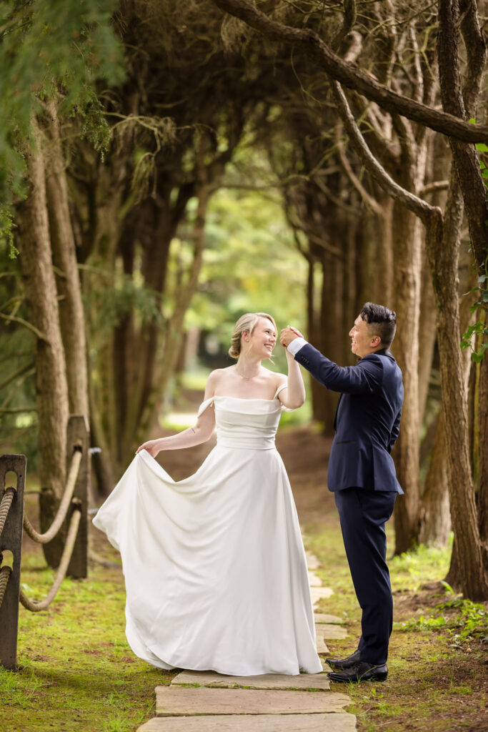 Bride holding up her dress dancing with the groom under trees at Old Westbury Gardens.