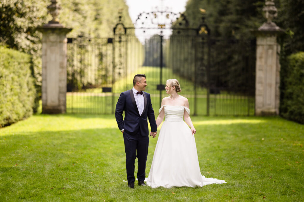 Bride and groom looking at each other while walking away from a very large gate at Old Westbury Gardens. 