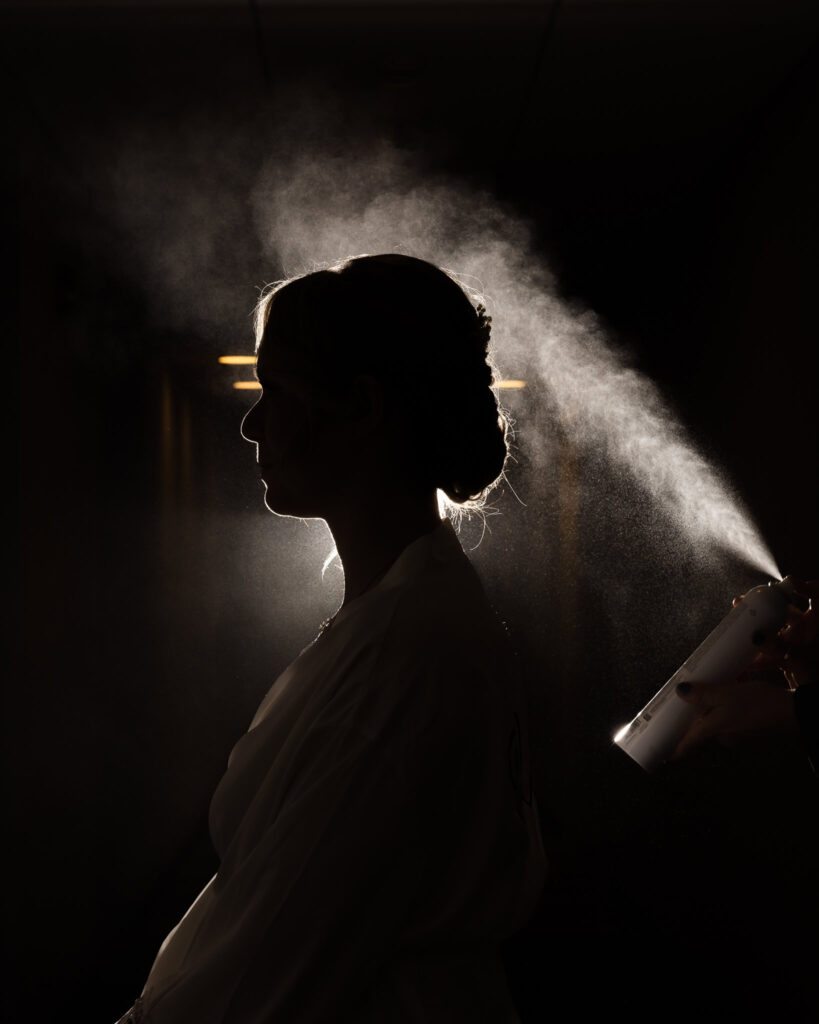 Silhouette of bride with black background with hairspray backlit. 