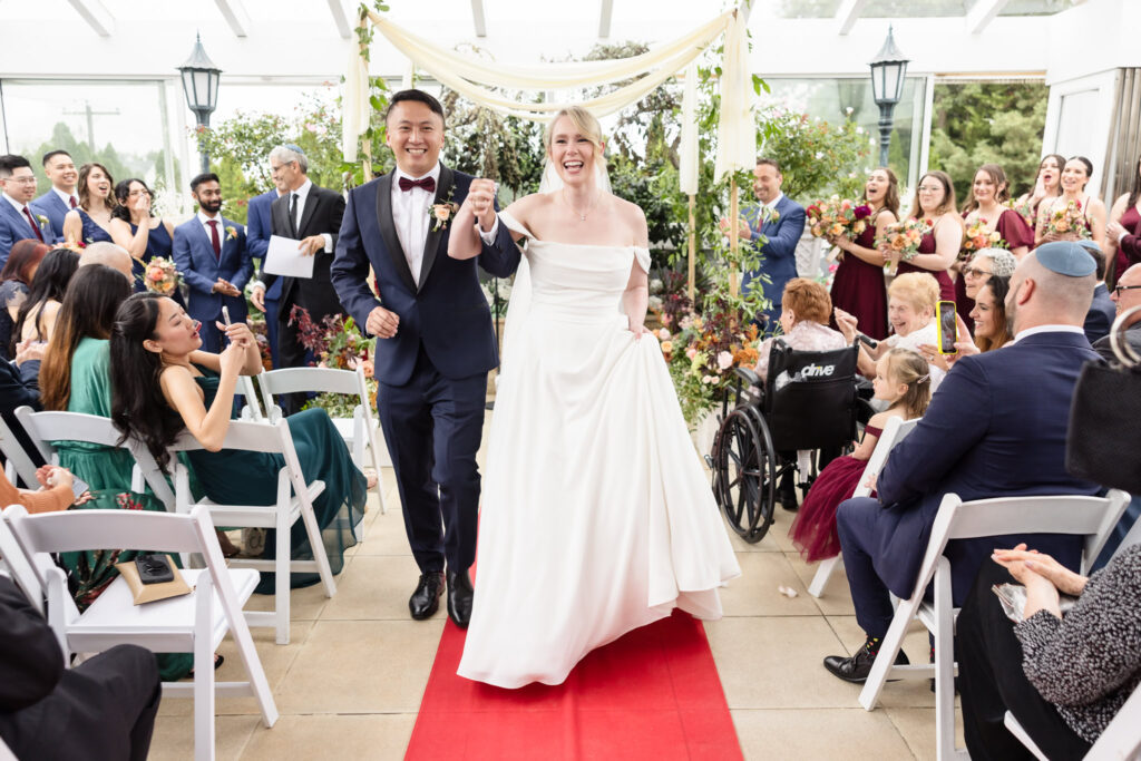 Bride and groom smiling as they walk down the aisle at Sand Castle Wedding Venue. 