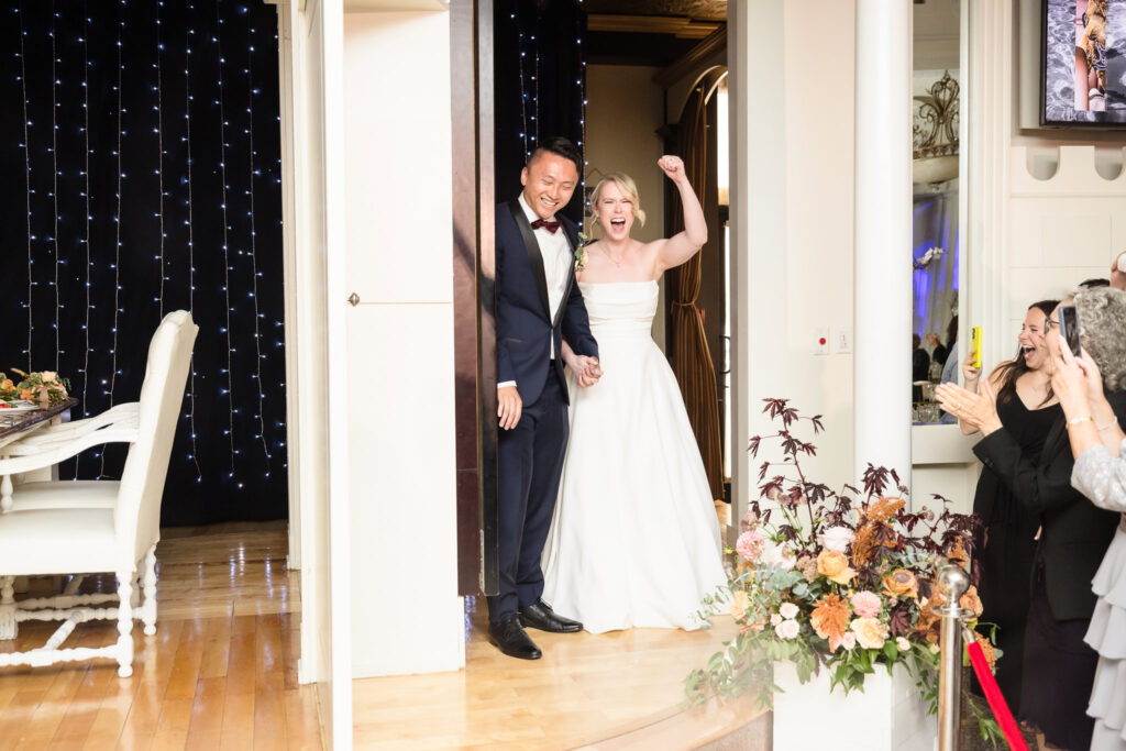 Bride and groom entering ballroom at Sand Castle. They are on a spinning platform and the bride is raising her hand in celebration. 