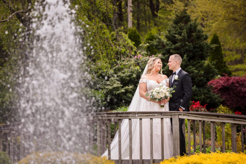 bride and groom looking at each other on bridge at East Wind Long Island with fountain in foreground.