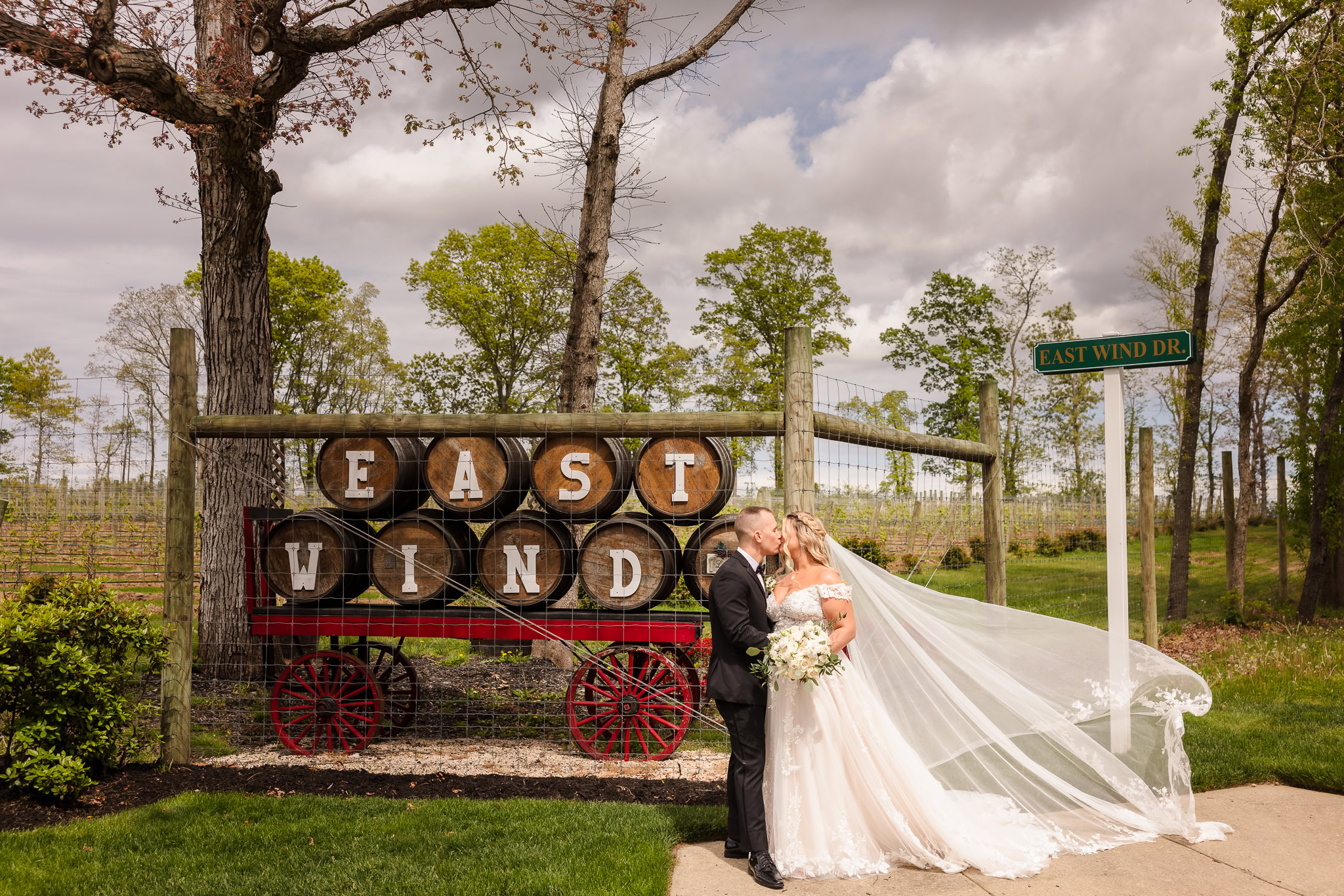 Bride and groom next to East Wind Long Island sign. The bride's veil is flowing out.