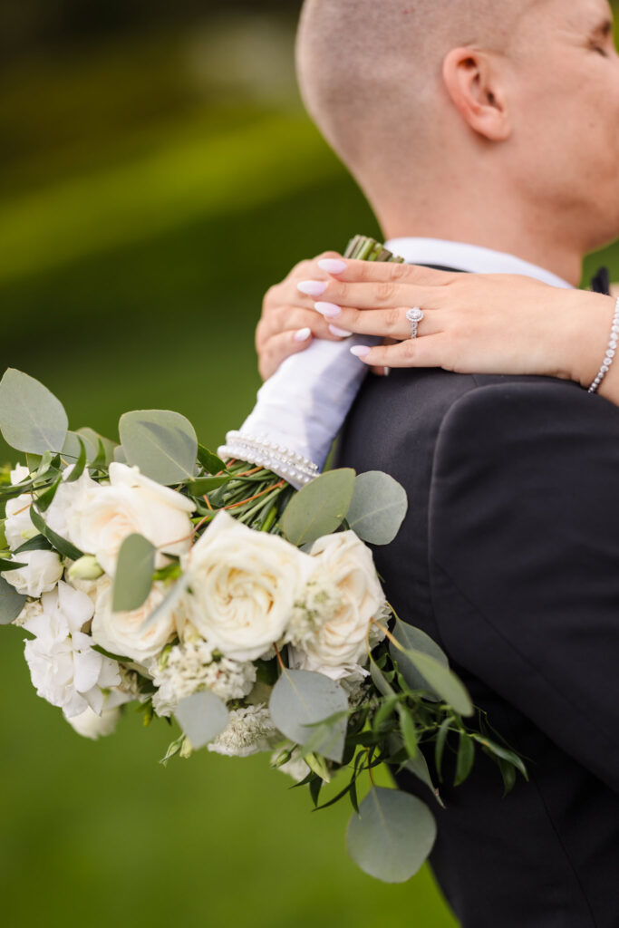 A close up photo of the bride's white bouquet being held behind the groom.