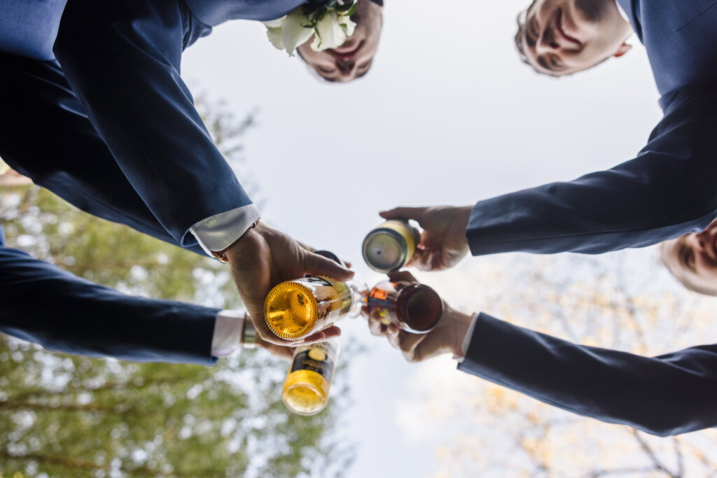 Groomsmen toasting beer at Crest Hollow Country Club. The image is taking from the ground look up to the bottom of the bottles. 