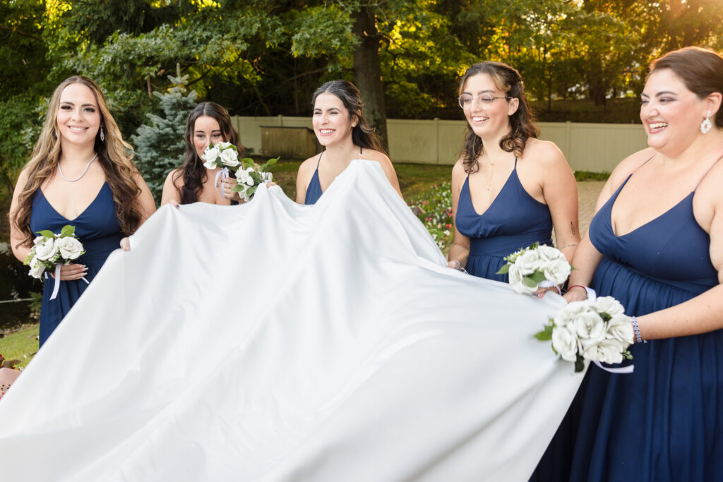 Bridesmaids adjusting the back of bride's dress at Crest Hollow Country Club. They are wearing blue and smiling. 