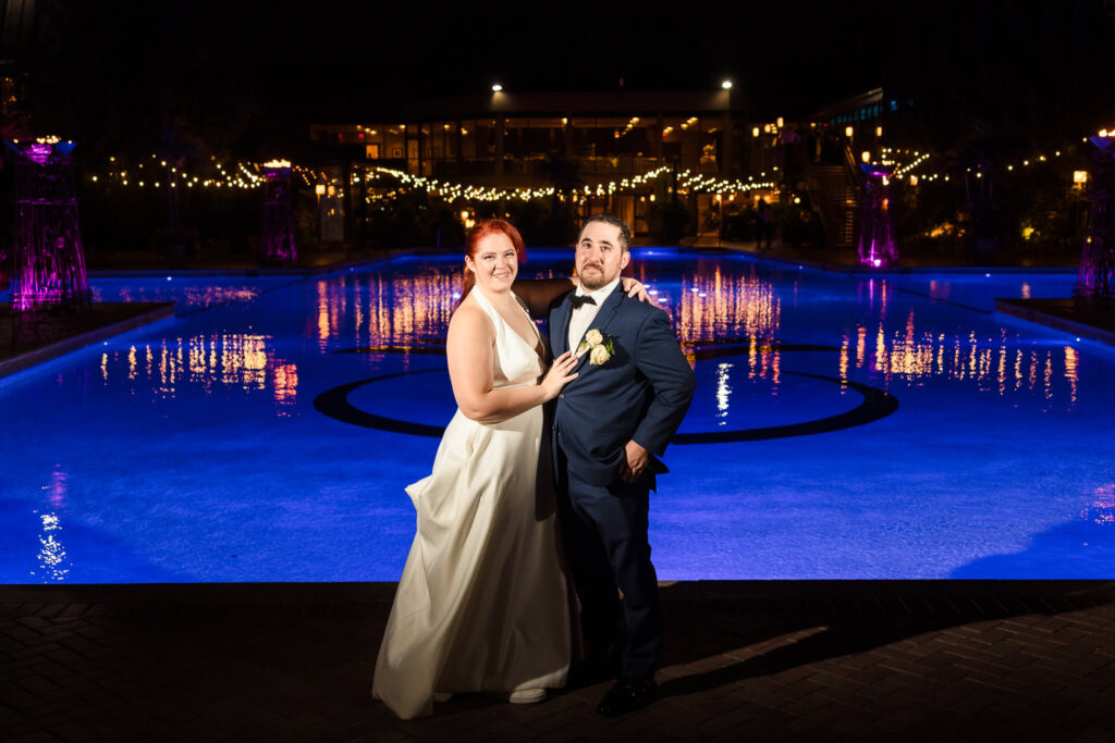 Bride and groom in front of pool at Crest Hollow Country Club. It is night, and the pool is lit up. 