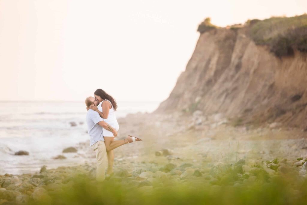 Man picking up woman and kissing by cliffs at Montauk Lighthouse State Park.