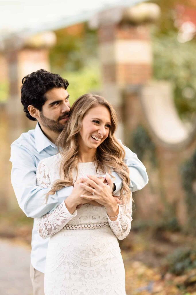 Man holding his fiance from behind at Old Westbury Gardens. 