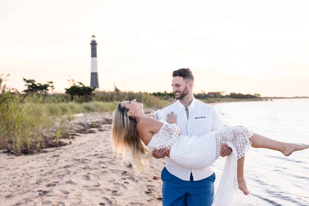 Man holding woman while they both laugh in front of the Fire Island Lighthouse.