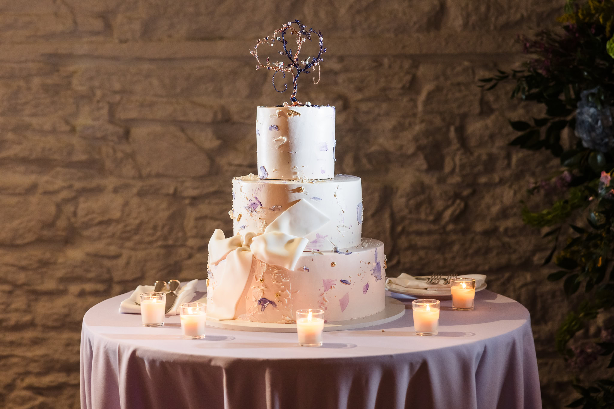 Wedding cake topped with two wire hearts and pieces of purple at Stone Mill at New York Botanical Garden wedding.