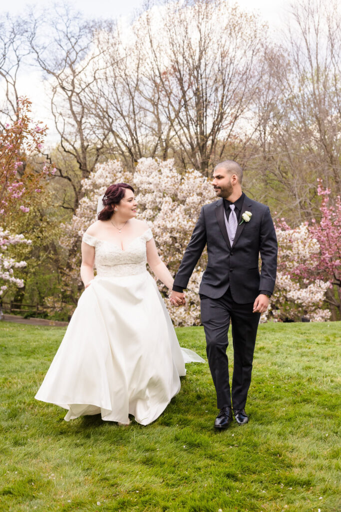 Bride and groom walking by blossoming cherry trees before their wedding at New York Botanical Garden.