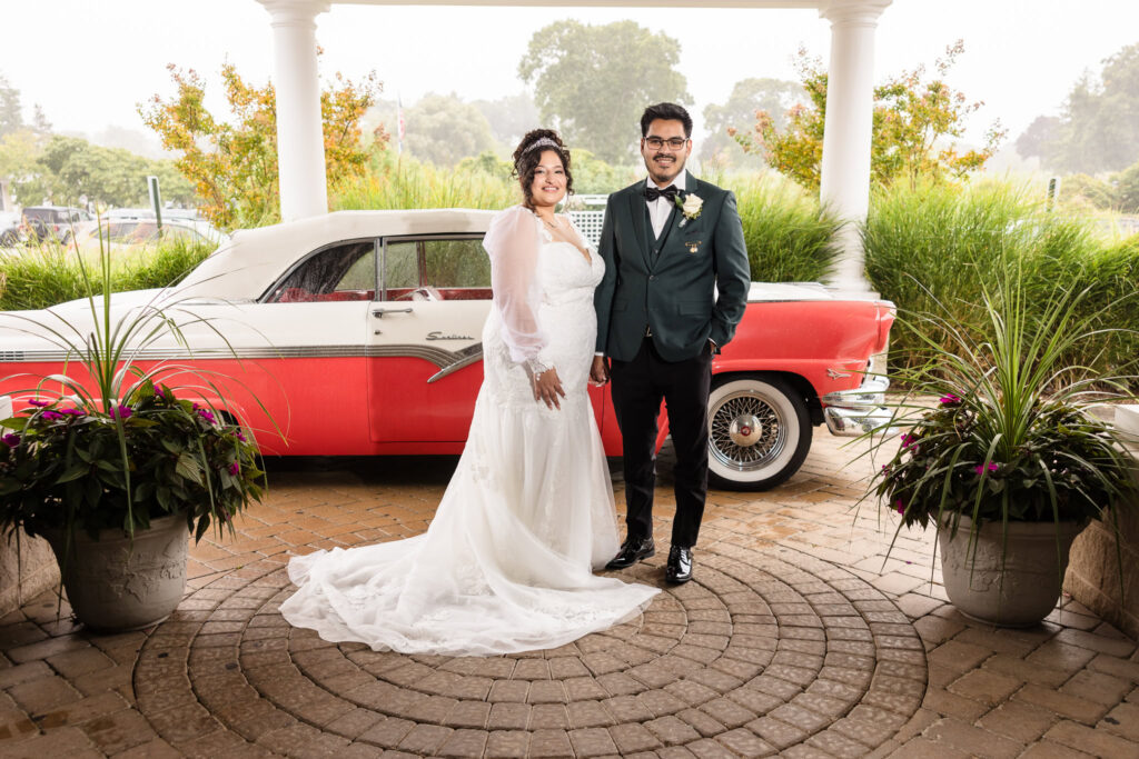 Bride and groom smiling at the camera in front of a classic car at The WaterV