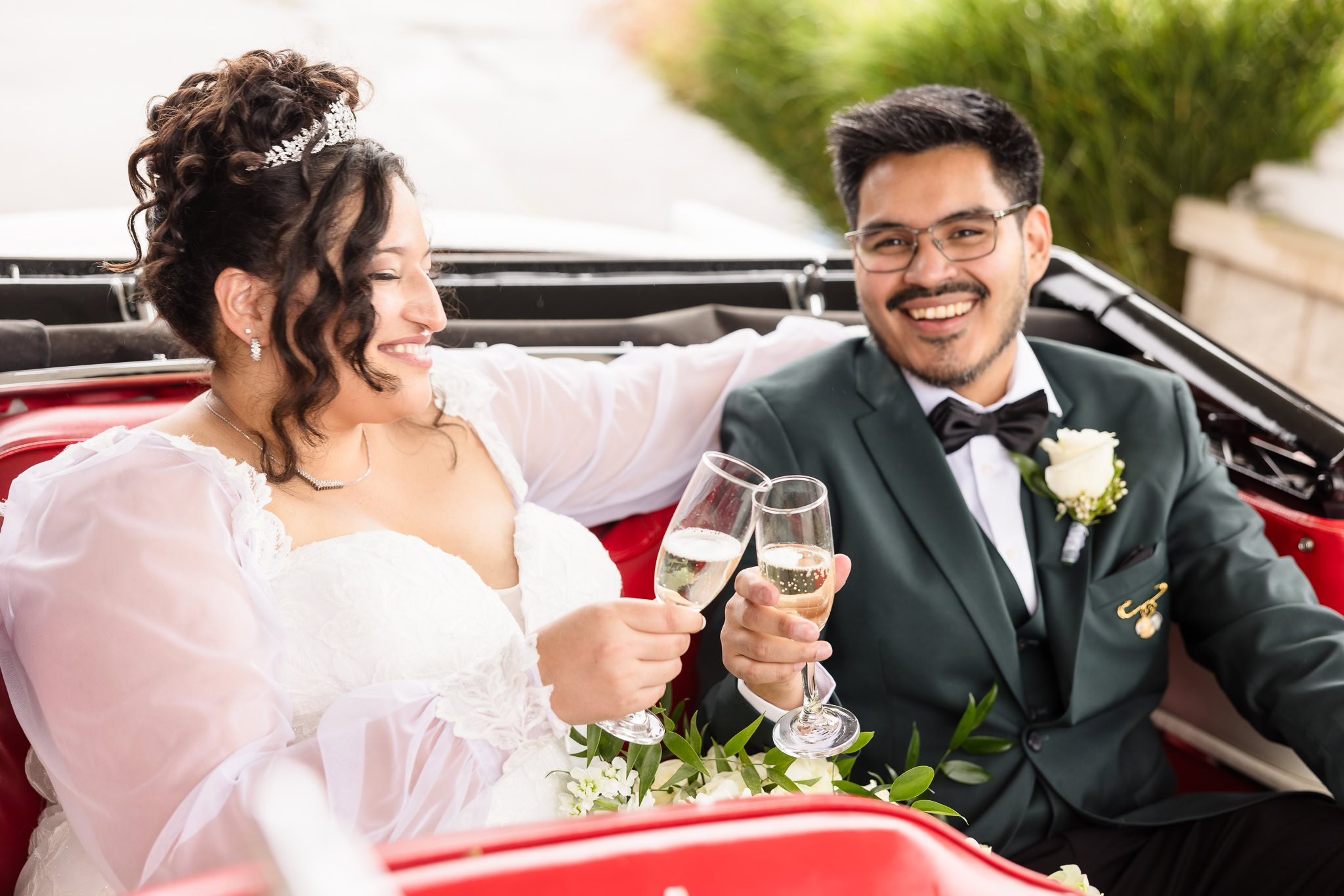 Bride and groom seated in classic convertible. They are toasting and celebrating.