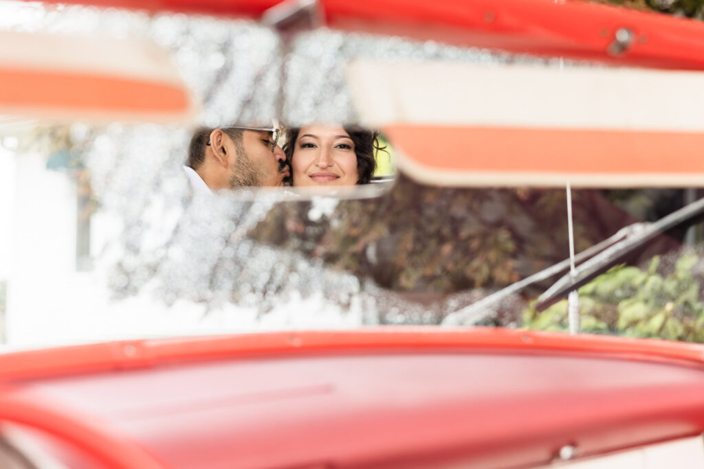 Groom kissing bride on the cheek seen through the rearview mirror of a classic car at WaterView.