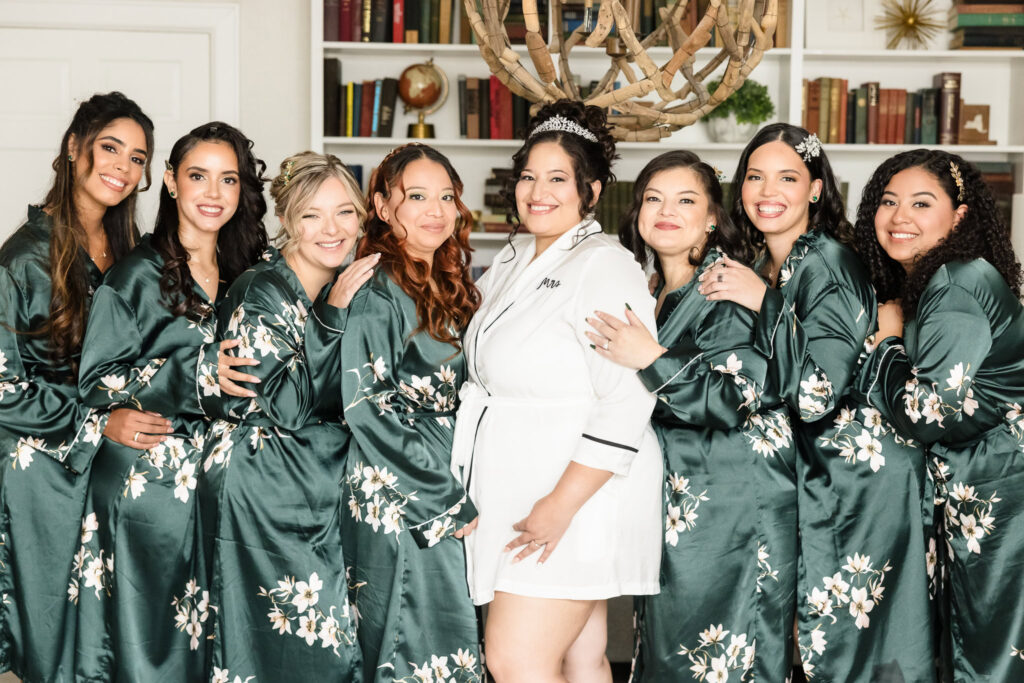 Bride with bridesmaids at Danford's Hotel. The bride is in a white robe. Everyone else is in a green robe with white flowers.