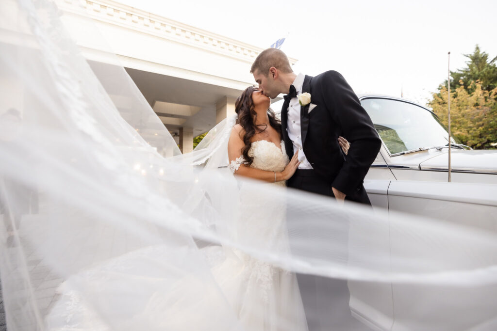 Bride and groom kissing with the veil of the bride coming toward the camera at the Garden City Hotel. 