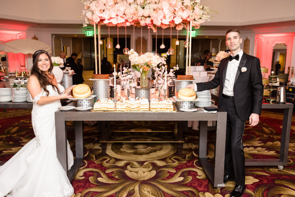 The bride and groom standing next to the desserts at The Garden City Hotel.