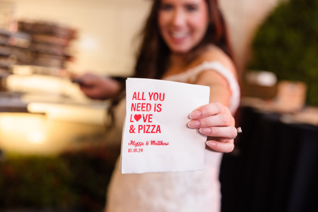 The bride holding up a napkin that says "All you need is love and pizza". 