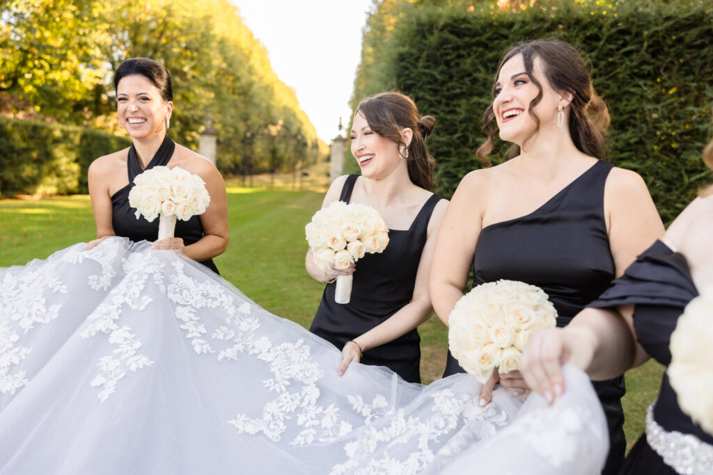 Bridesmaids at Old Westbury Gardens laughing while they play with the bride's dress. 