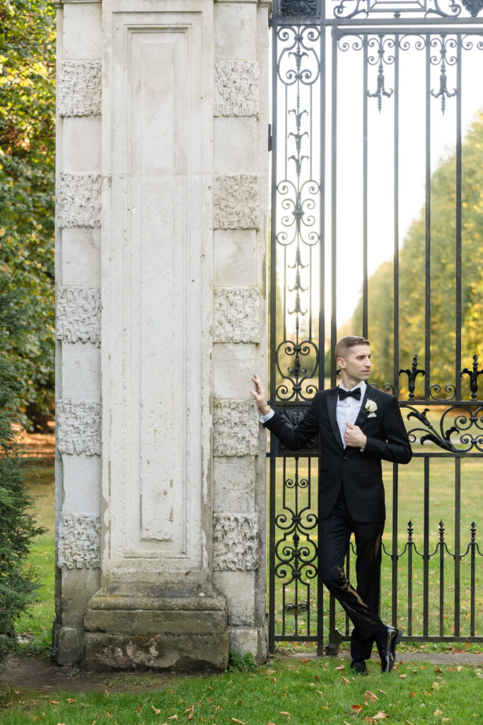 Groom standing next to pillar and looking away at Old Westbury Gardens.