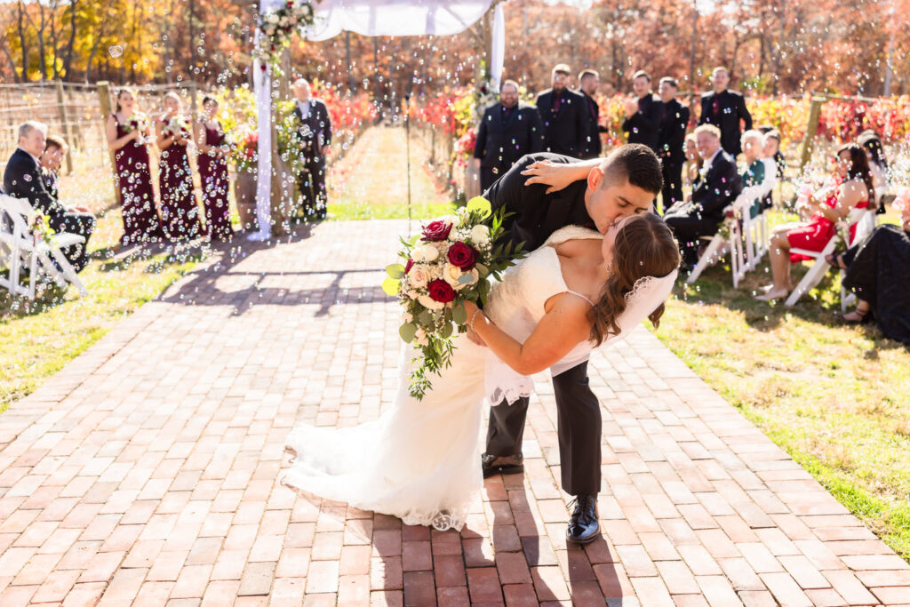 Bride and groom kissing after ceremony with bubbles and guests behind them.