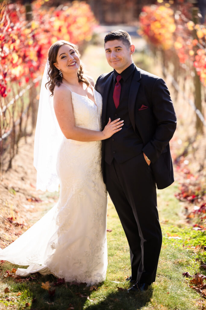 Bride and groom smiling at the camera while standing in the vineyard.