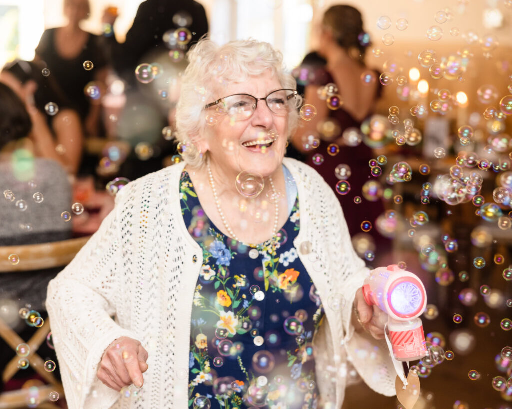 Bride's grandmother laughing while using a bubble gun and dancing at The Vineyard at East Wind Long Island. 