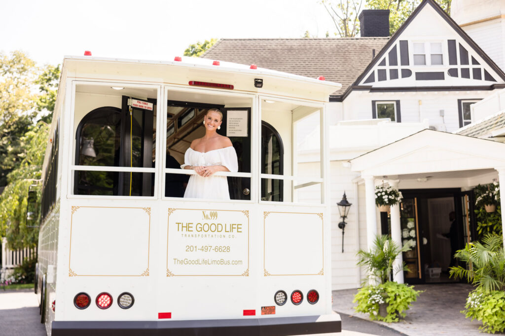 Bride standing at the back of a white wedding trolley outside Sea Cliff Manor, with the manor's white-and-black exterior visible behind her.