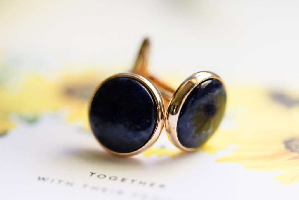 Blue cufflinks on top of wedding invitation.