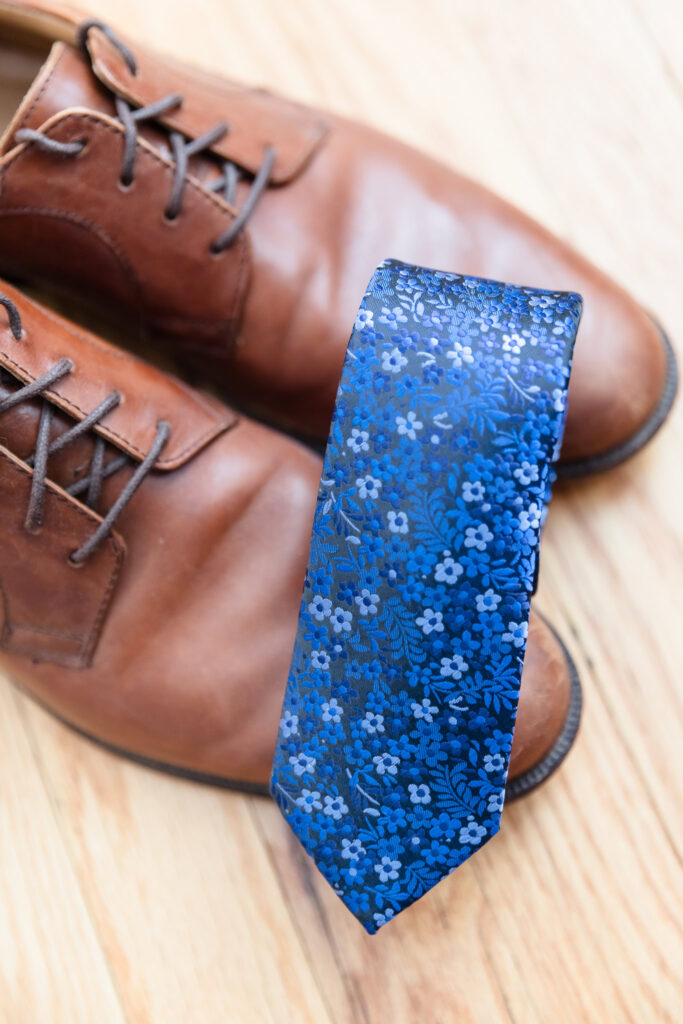 Groom's shoes with blue tie on top of shoes. 