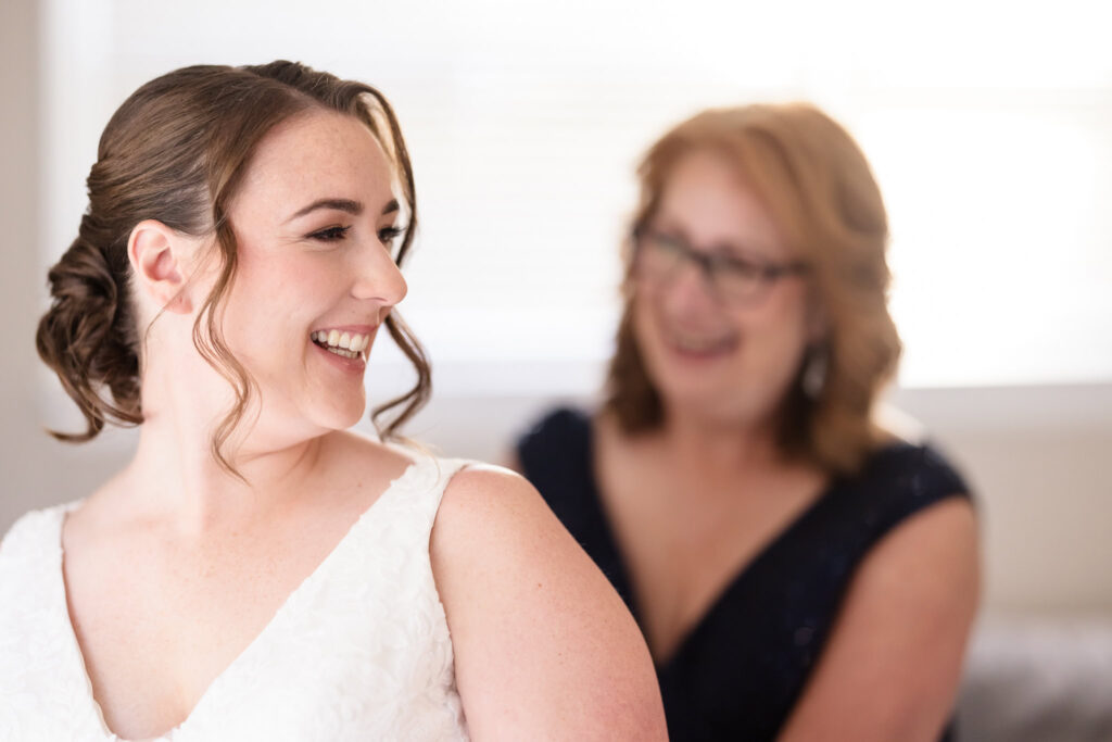 Bride smiling while her mother smiles as zipping up her dress.