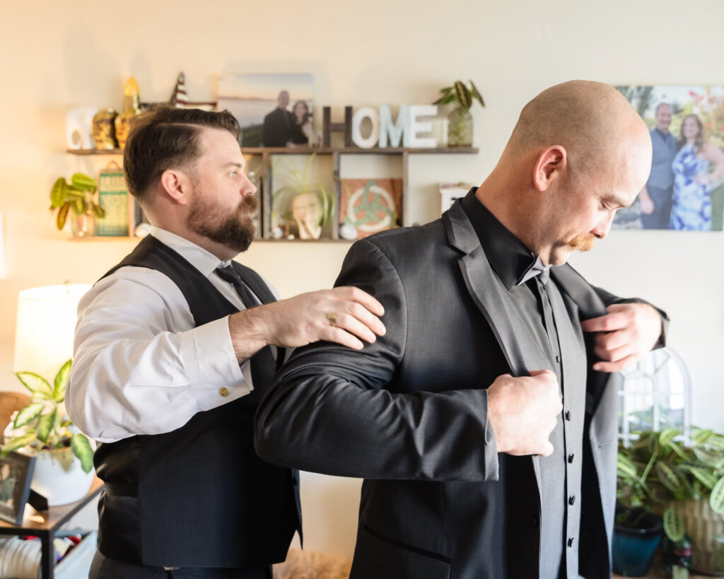 Best man helping groom put on his jacket. 