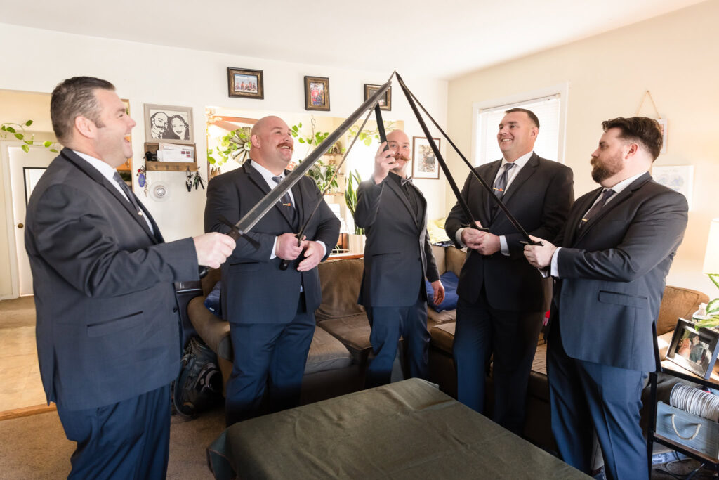 Groom and groomsmen holding swords towards the ceiling. 