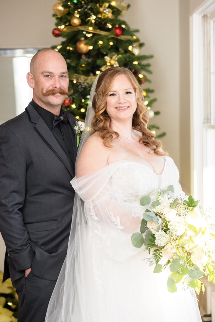 Bride and groom taking a portrait in front of a Christmas tree at Stewart Manor Country Club.