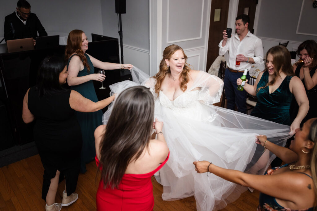 Bride's dress being held by others as she dances in a circle. 