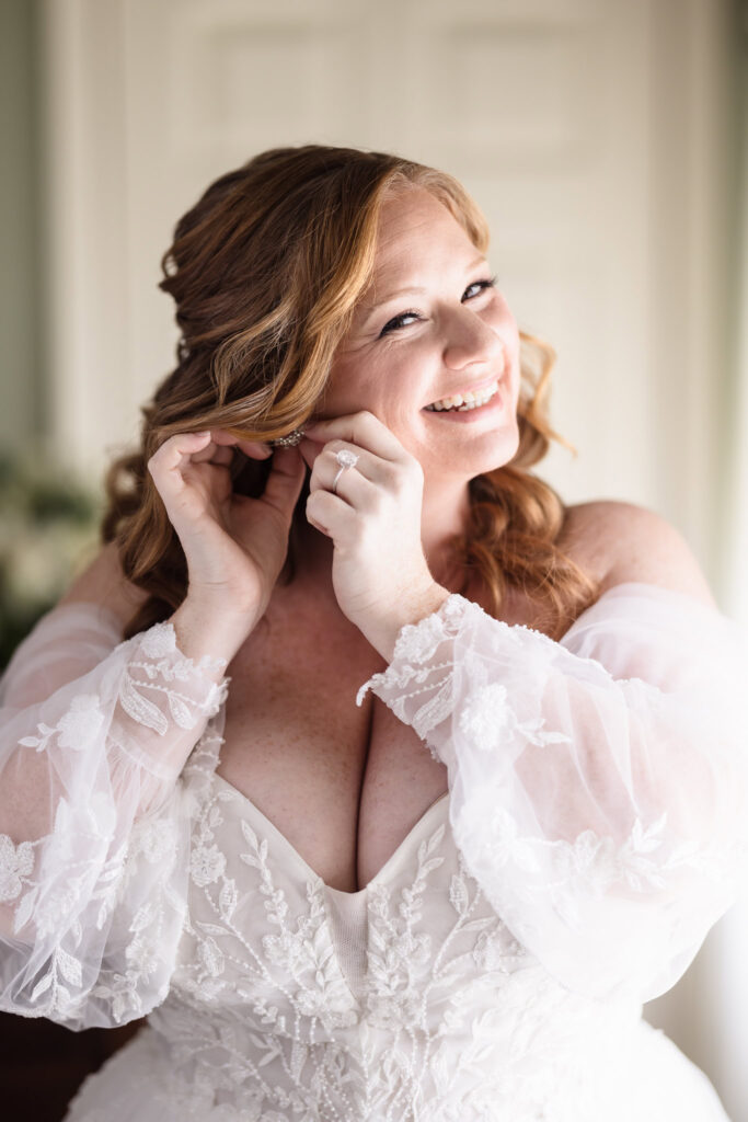 Bride putting on her earrings and smiling at the camera.