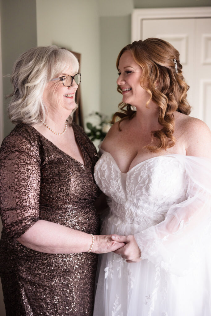 Bride and her mom holding hands and smiling at each other. 