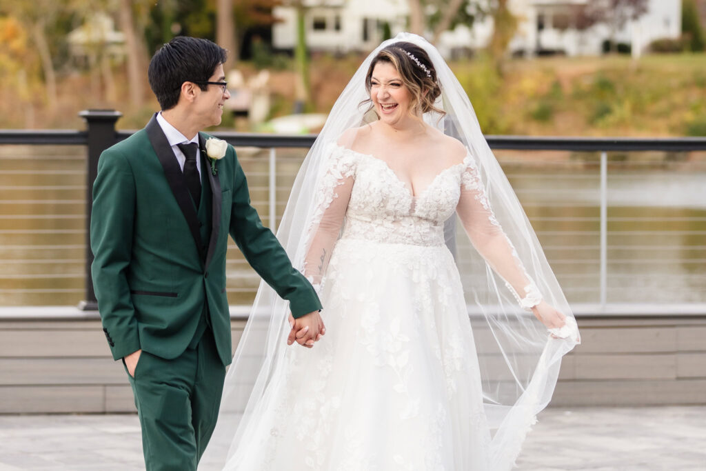 Bride and groom holding hands and smiling as they walk together at Water's Edge.